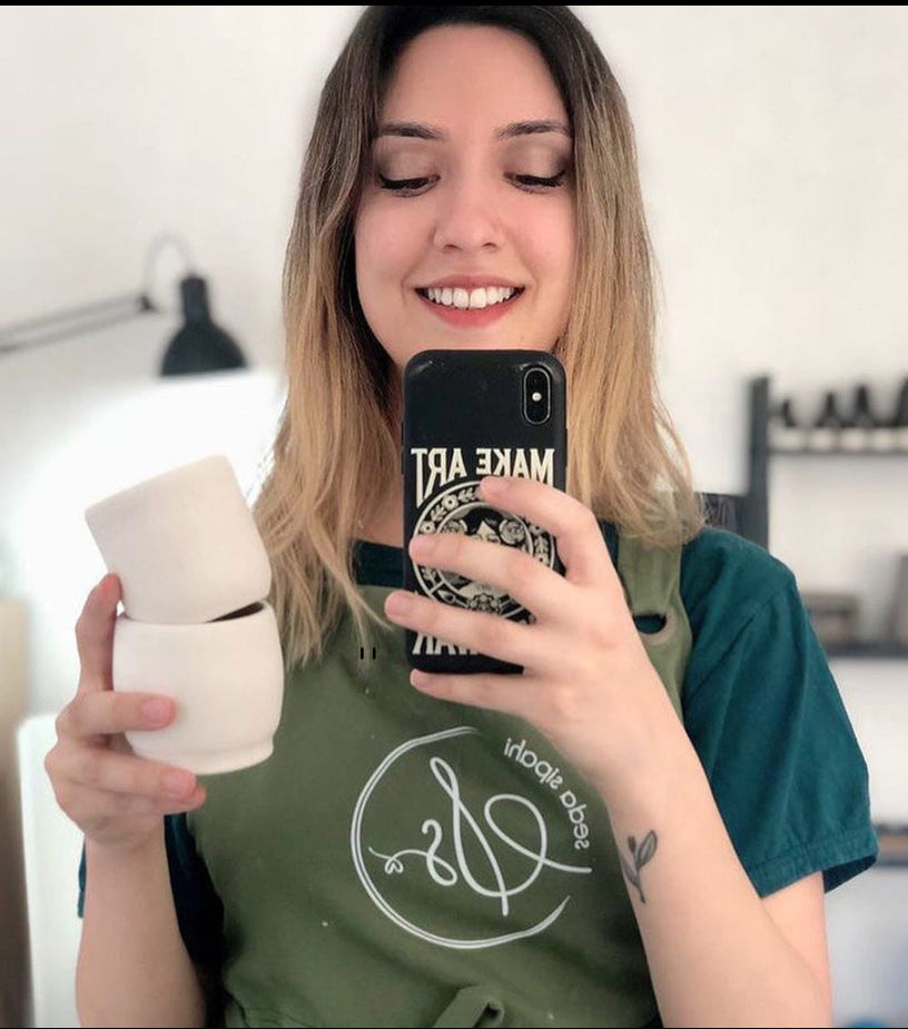 Logo baskılı yeşil önlüğüyle ayna selfiesi çeken seramik sanatçısı