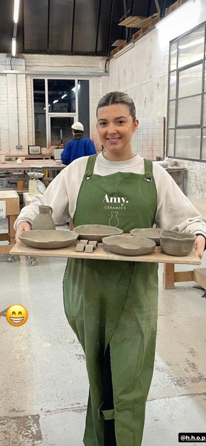 Amy Ceramics logolu yeşil önlükle seramik tabak tepsisi taşıyan usta